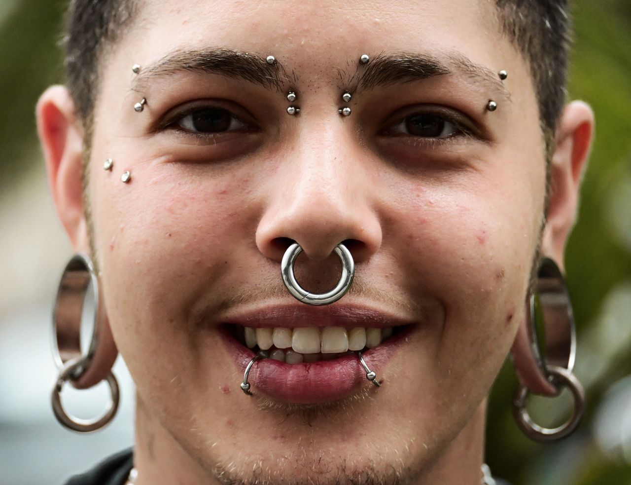 Close-up portrait of a young man showcasing a variety of unique facial piercings and jewelry.