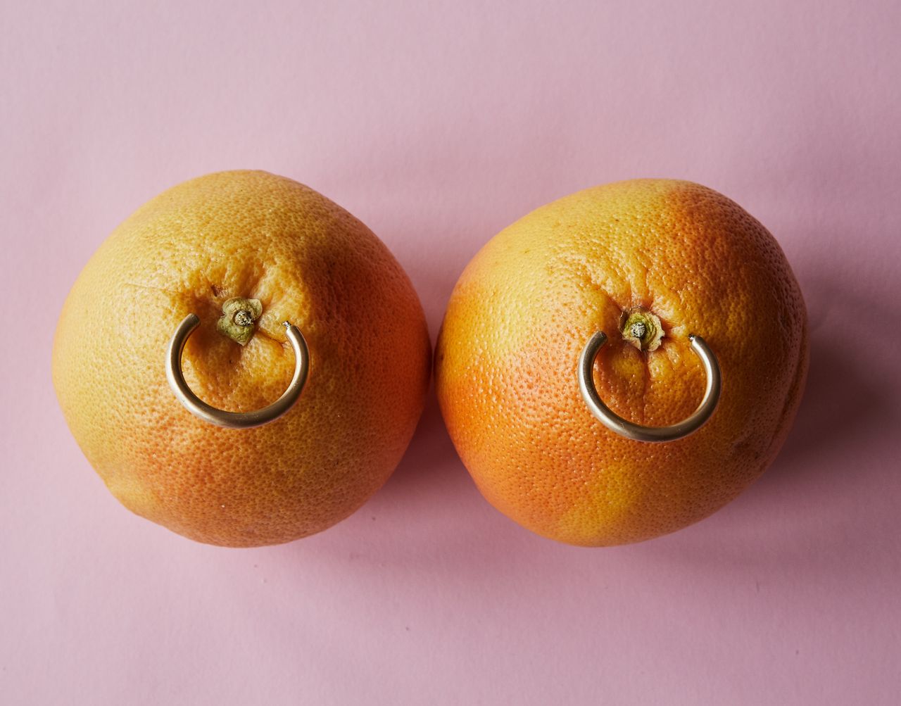 Top view of ripe oranges with golden earrings against pink background advertising jewelry