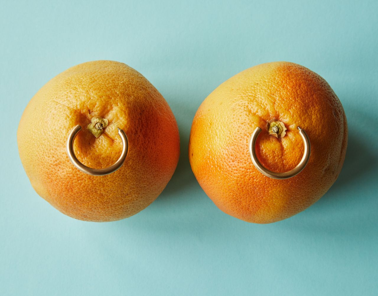From above of fresh ripe oranges with golden earrings as advertisement of accessories placed on blue surface in studio